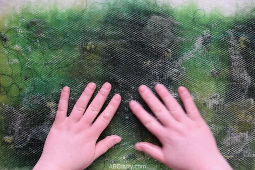 Rubbing hands over green wool and other fibers covered in mesh fabric