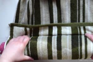 Tucking the end of a towel with green stripes under the edge of a pool noodle that it's wrapped around