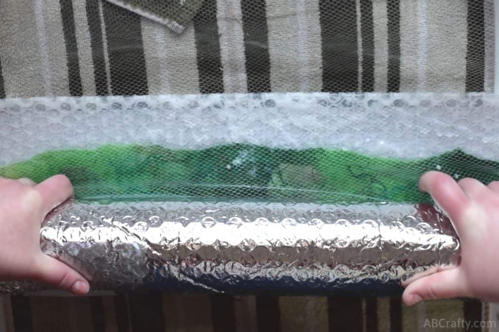 Rolling partially felted green wool in bubble wrap with mesh fabric on top and a towel underneath