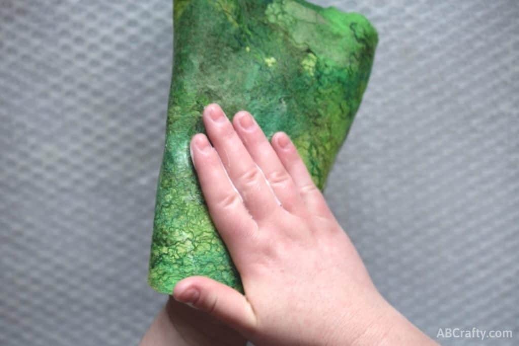 Palming prefelt green wool with fun green swirls and designs. Holding soapy fabric between both hands