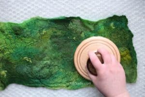 Using a heartfelt silks palm washboard on top of a green wool piece of prefelt to help full and felt the wool