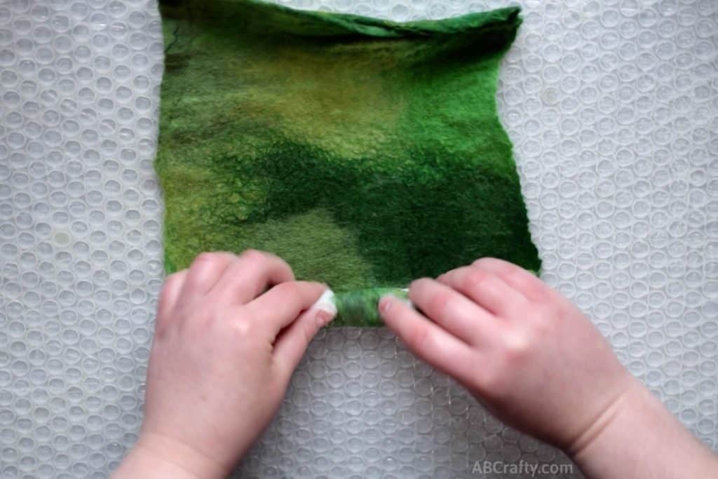 Rolling the edge of partially felted green handmade felt