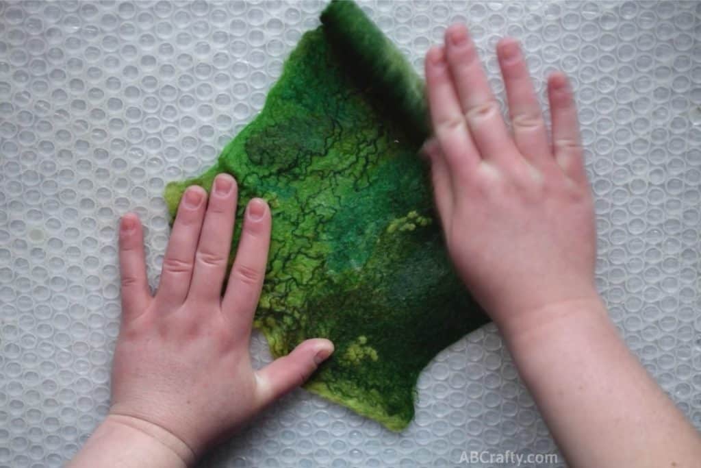 Vigorously unrolling green partially felted green wool fabric from one end