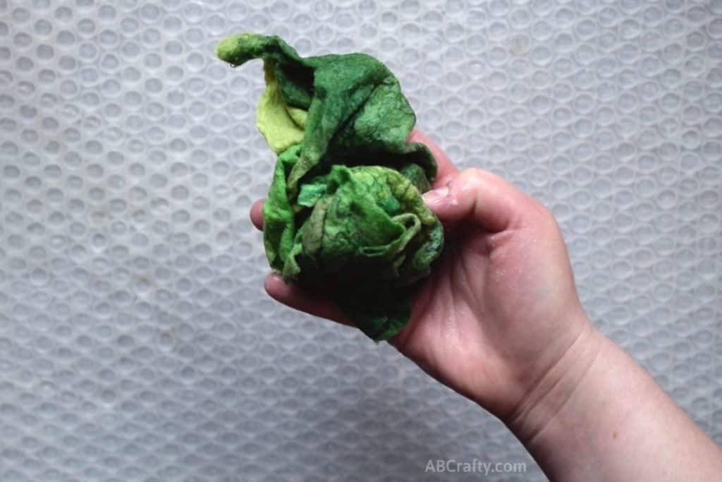 Green wet and soapy wool fabric that has been partially felted wadded up in a ball in a hand