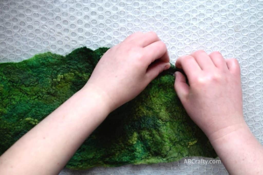 Pinching and rolling the corner of partially wet felted green artful felt fabric