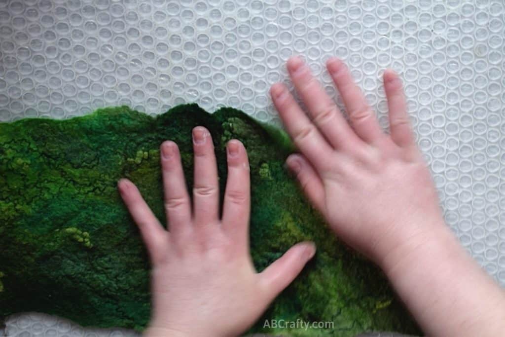 Unrolling and shaking corner of green prefelt wool fabric on top of bubble wrap