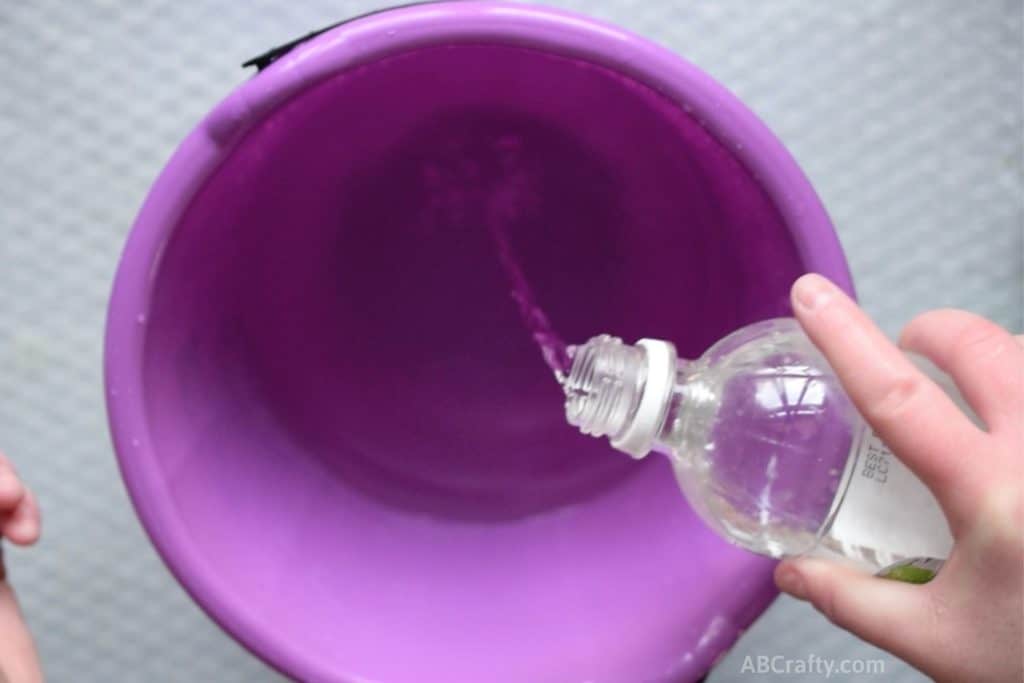 Pouring vinegar into a plastic purple bucket filled part way with water