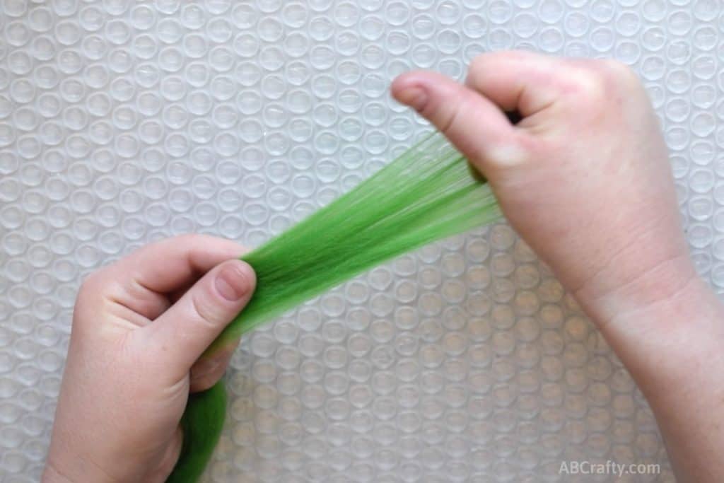 Holding green wool roving in one hand and with the other, pulling a small amount of the fiber away