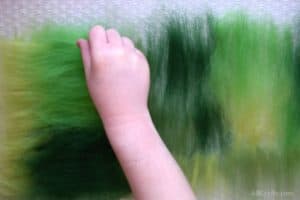 Placing small amounts of green wool roving perpendicular on top of different colors of wool roving that are on top of bubble wrap