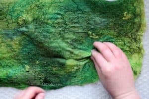 Performing pinch test on prefelt wool that is partially wet felted green wool with various fibers felted into the wool