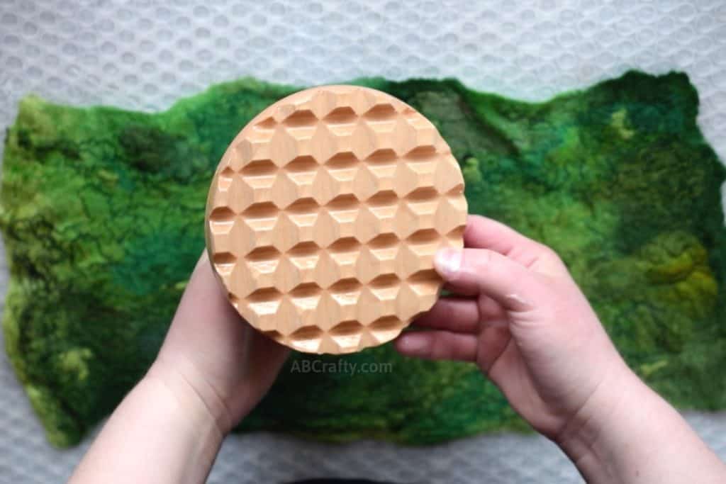 Showing the bottom of a palm washboard from Heartfelt Silks on top of a wet felted piece of green wool fabric