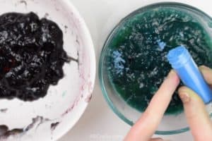 shaking blue edible glitter over greenish blue diy slime with purple diy slime in a bowl next to it