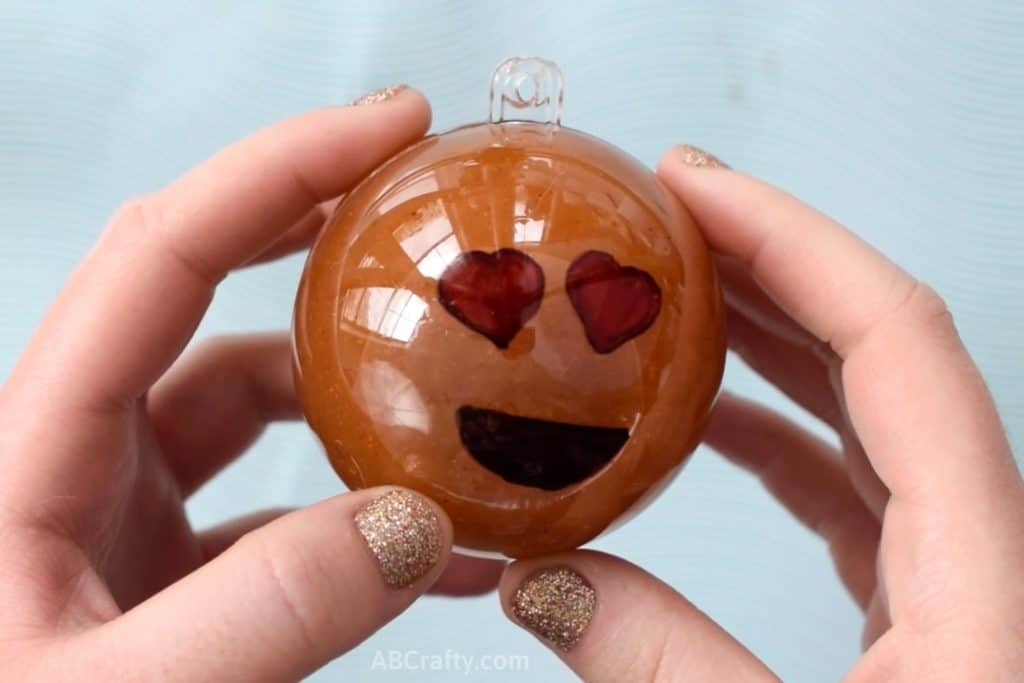 Holding a plastic ornament with a heart eye emoji on it filled with orange