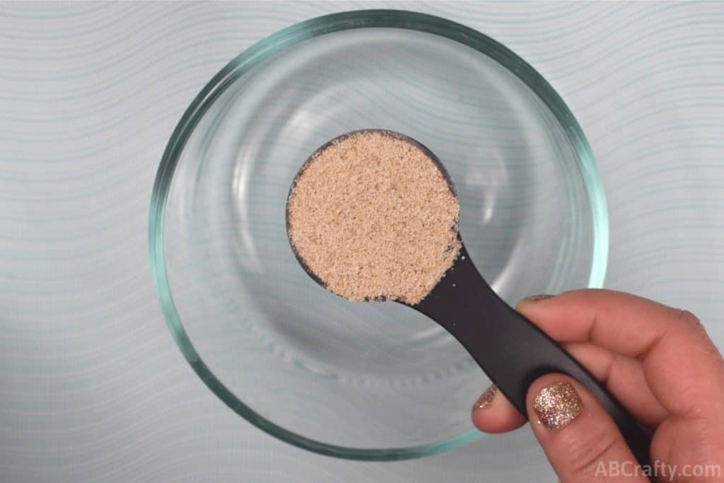 Holding a tablespoon of light brown fiber powder over a clear glass bowl