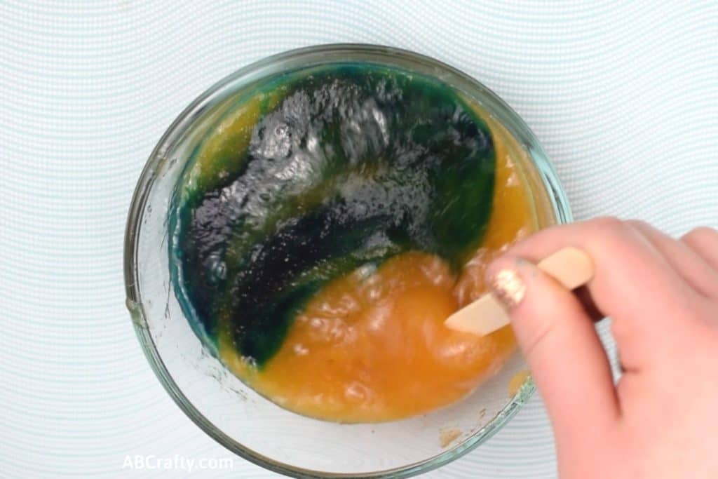 Stirring blue food dye into orange edible slime turning it blue