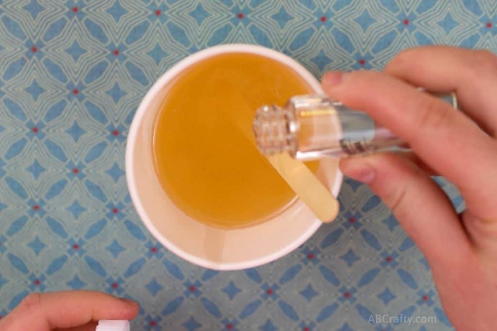 Pouring essential oils into melted soy wax that's in a paper cup with a popsicle stick in it