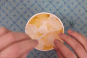 Placing an ice cube on top of melted wax with ice cubes throughout, while holding a candle wick in the middle of the wax