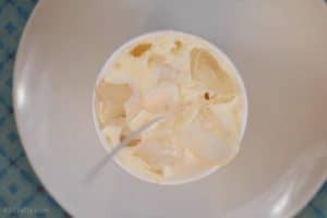 White soy wax in a paper cup cooling around ice with a candle wick in the middle.