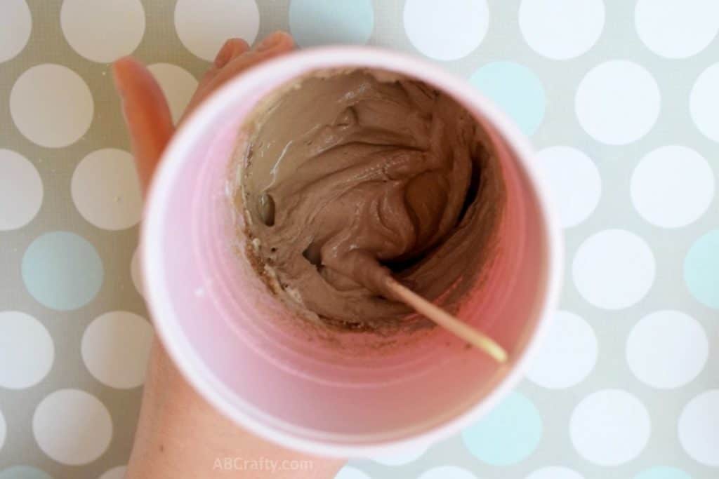 popsicle stick mixing a thick brown chalk mixture with a popsicle stick in a cup