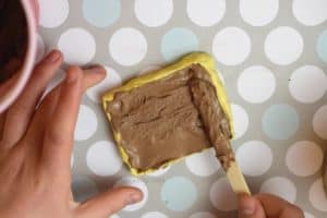 spreading wet brown chalk mixture with a popsicle stick into a yellow silicone mold