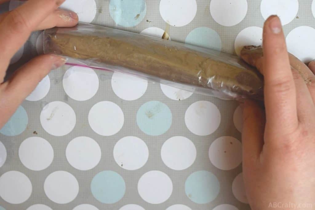 rolling a ziplock bag around a brown chalk paste mixture in the shape of a log in a plastic bag