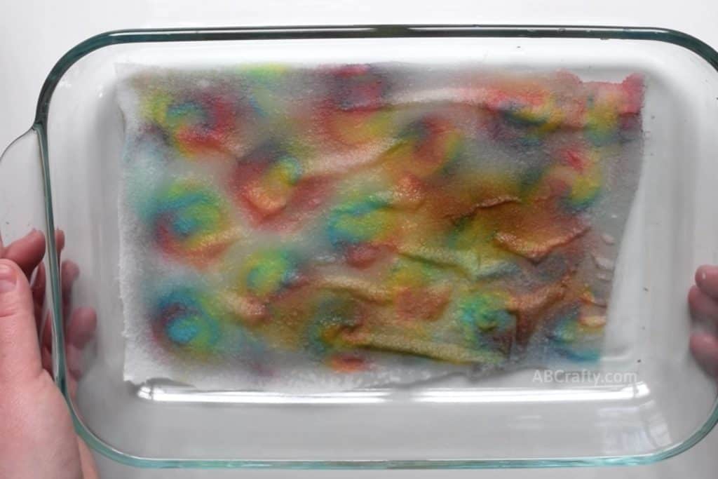 Rainbow silk fabric with circles of rainbow inside a pyrex dish. Some of the fabric has been burnt as the sugar has caramelized from the candy getting too hot