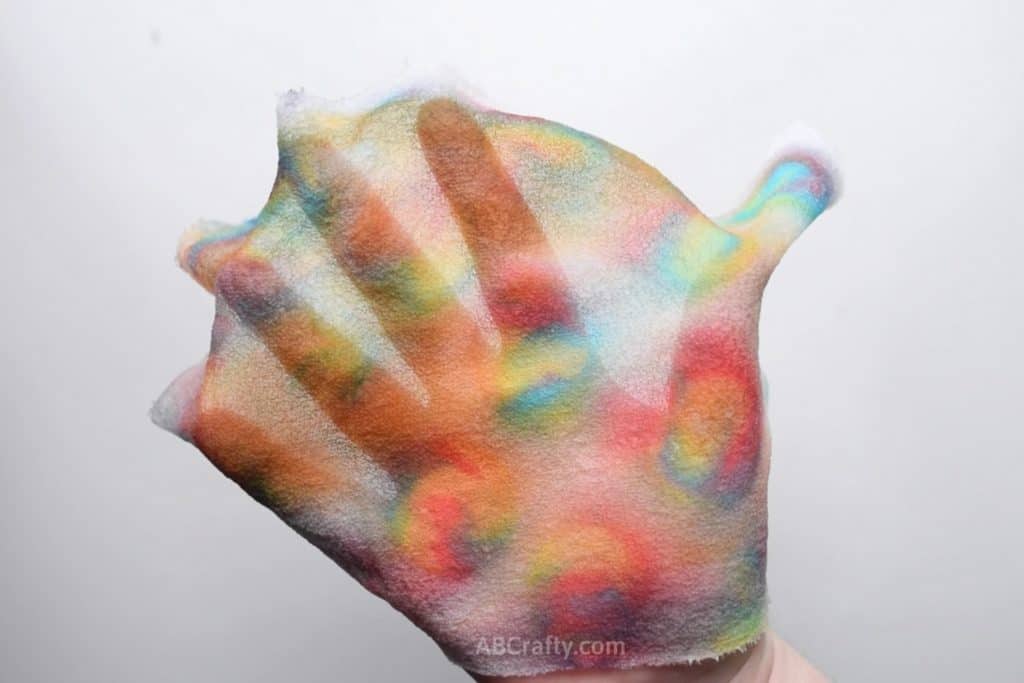 A partially see through piece of silk fabric with spirals of colors draped on a hand