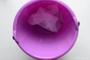 Piece of habotai silk fabric scrap soaking in water and vinegar in a purple bucket