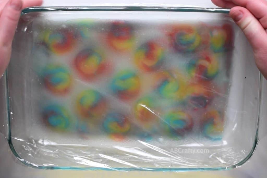 Placing plastic wrap over a pyrex dish containing silk fabric that has swirly lollipop prints, leaving a tie dyed effect
