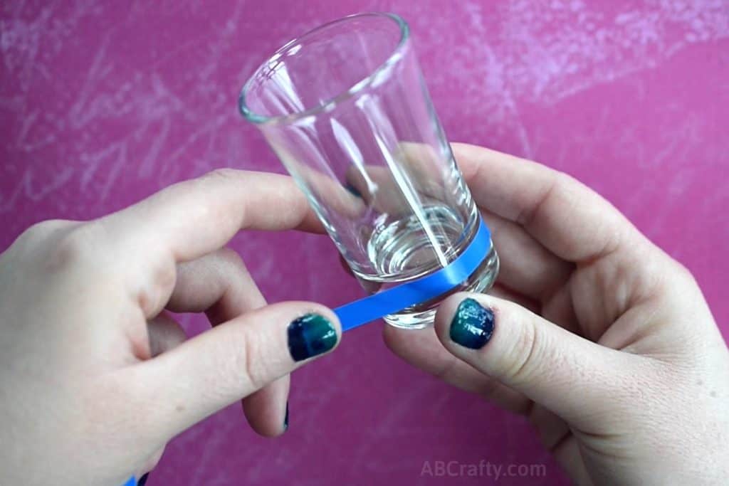 Placing blue vinyl design tape around the bottom of a shot glass to form a stencil