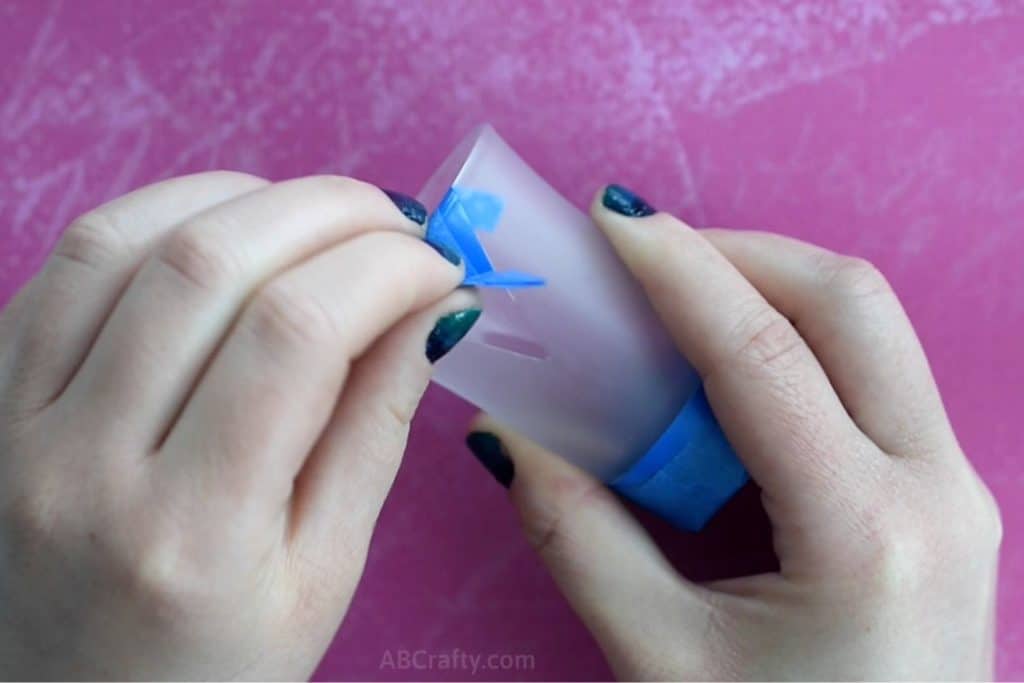 Pealing blue painters tape and blue vinyl tape off of a shot glass that has been frosted by hand