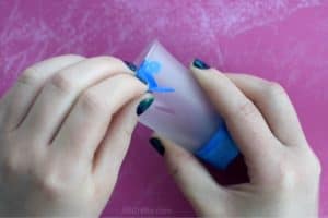 Pealing blue painters tape and blue vinyl tape off of a shot glass that has been frosted by hand