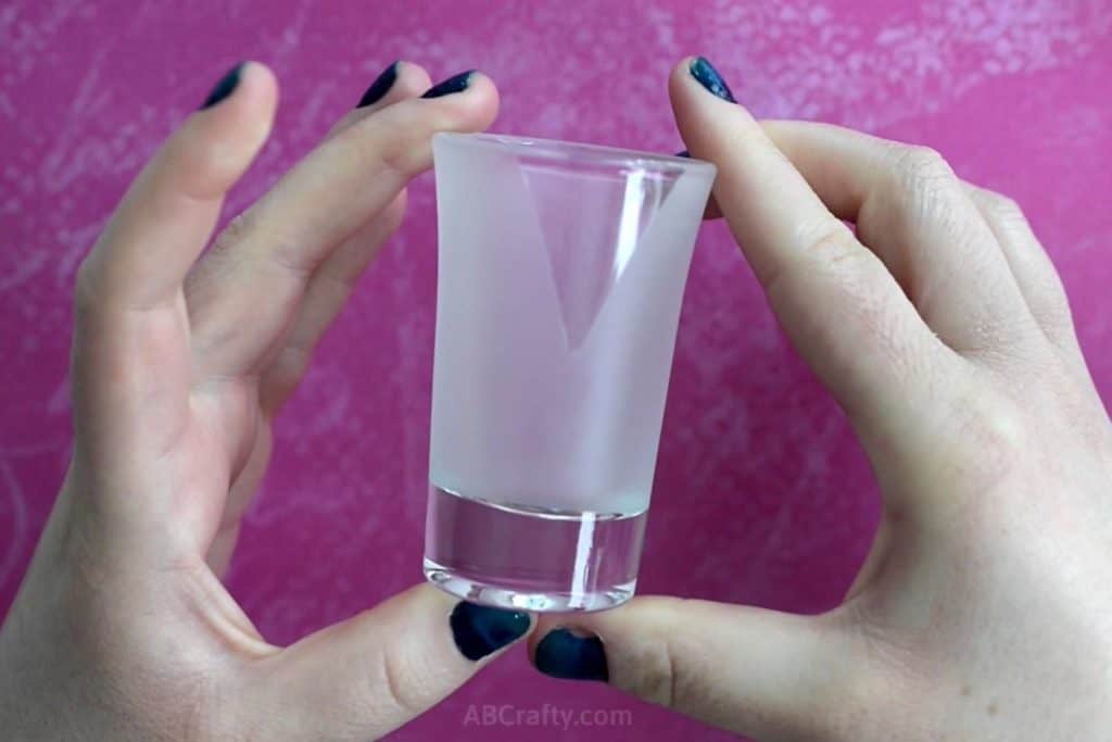 Holding a shot glass that has been frosted with a clear triangle at the top