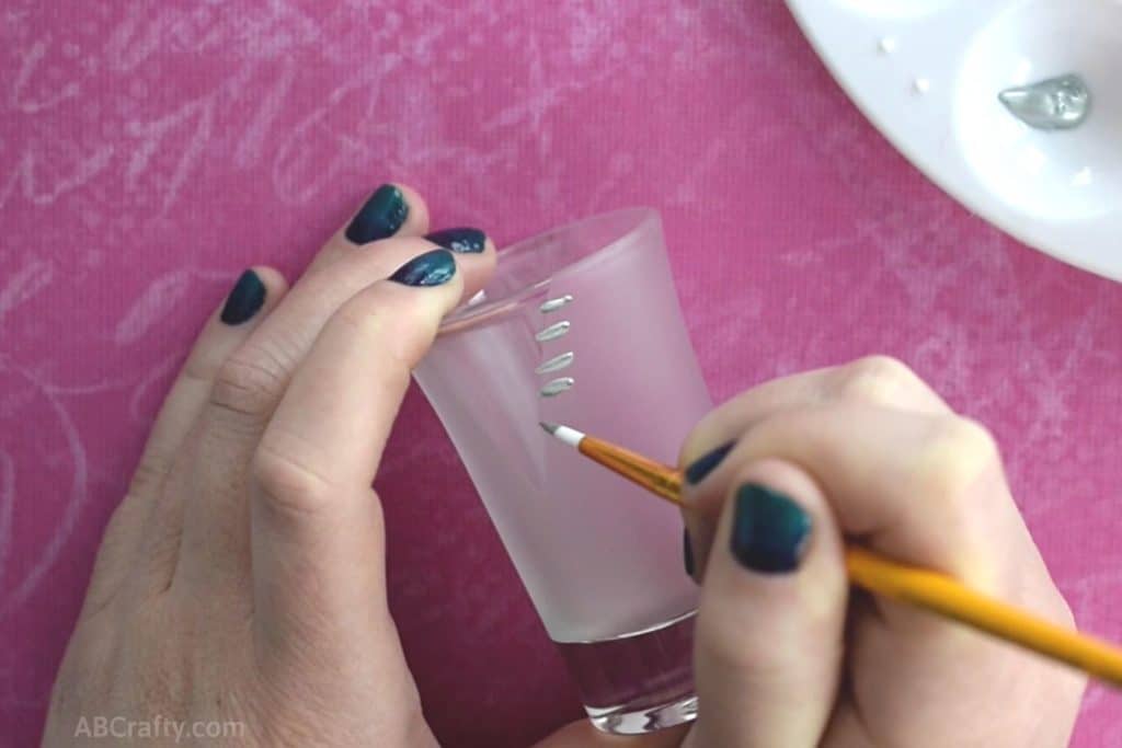 Starting to paint a zipper design onto a shot glass using silver acrylic paint