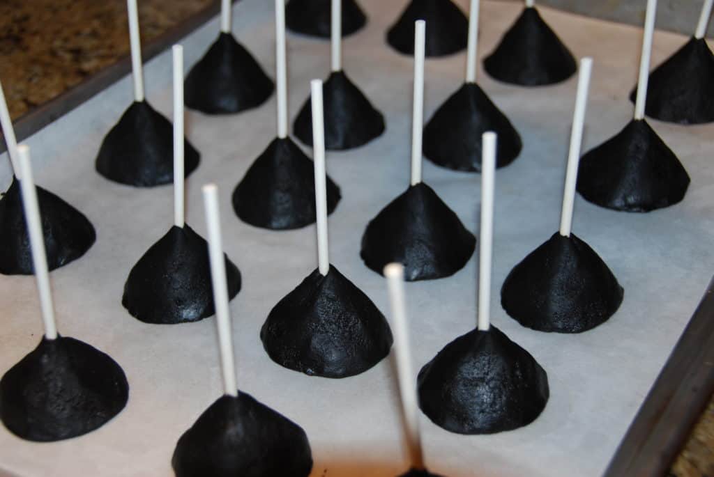 Oreo truffles in the shape of cones with lollipop sticks stuck into the more narrow side on a sheet pan covered in parchment paper