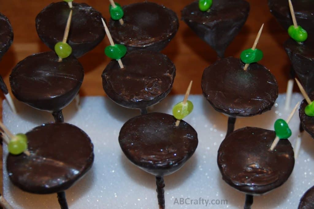Edible martini glasses made of chocolate and dusted with edible glitter with a toothpick and jelly bean as an olive. The bottoms are made of lollipop sticks and are pressed into a cake pop stand