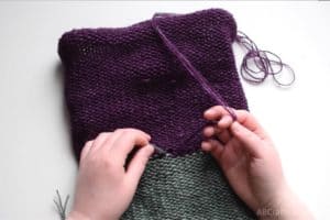 With the purple and green knit tube inside out, tying the ends of each color together in a knot