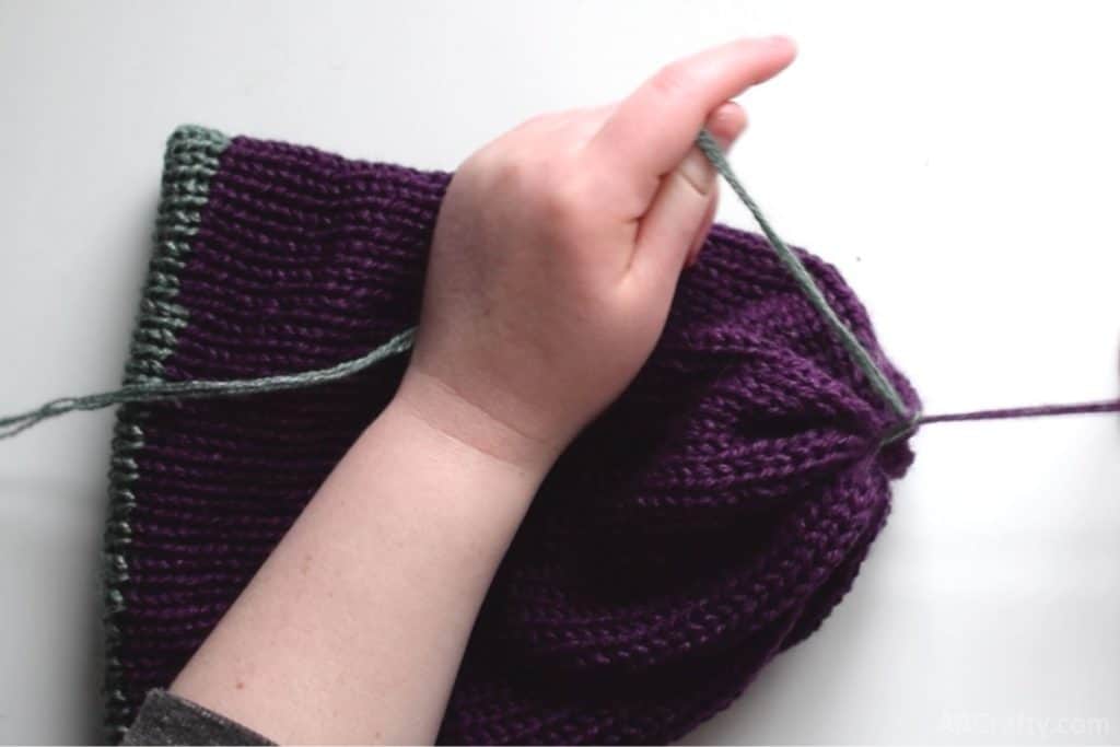 tying the ends of the purple and green yarn together so that the purple end closes up