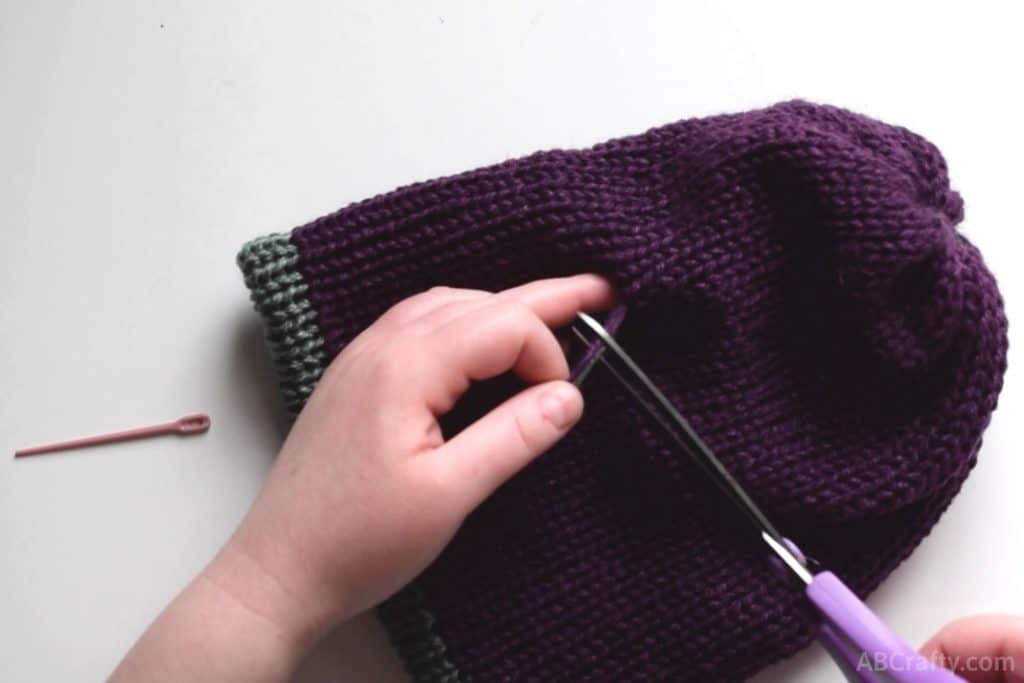 cutting the end of the yarn after sewing it into the middle of the knit hat