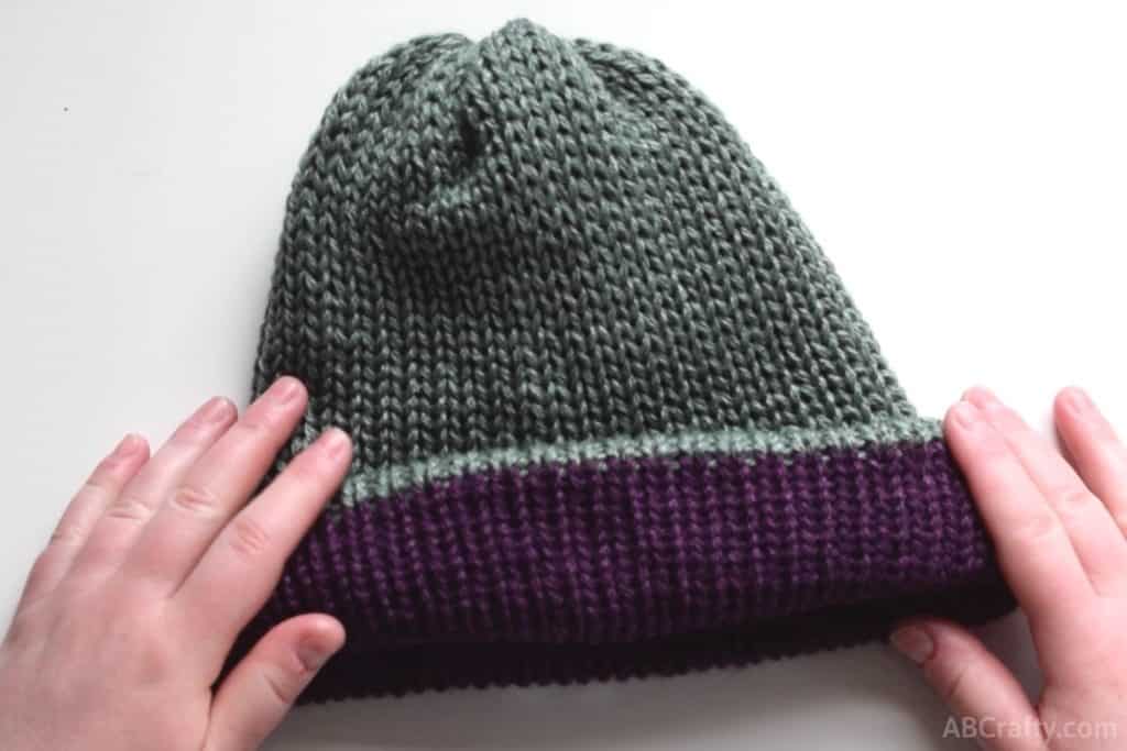 rolling the reversible knit hat part way inside out so the purple from the inside shows, giving the green hat a purple brim