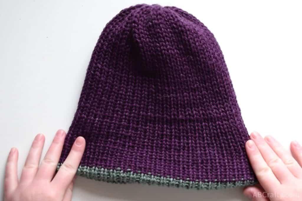 holding the handmade knit beanie with the purple side facing out