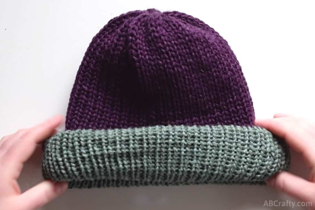 rolling the brim of the knit beanie so the green from the inside is facing out on top of the purple