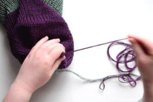Pulling on purple yarn to close the end of a reversible knit beanie