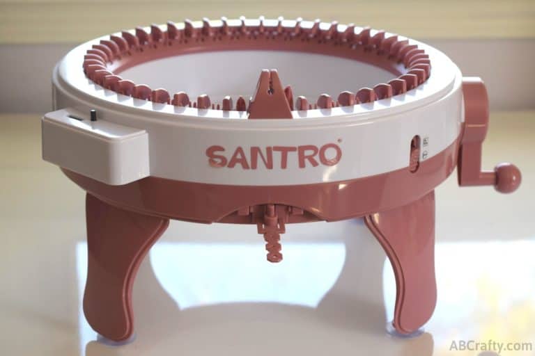 Pink and white hand crank Sentro knitting machine with row counter on a white table but the label reads "santro"