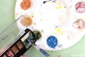 scraping green eyeshadow out of a profusion eyeshadow palette into a mixing palette