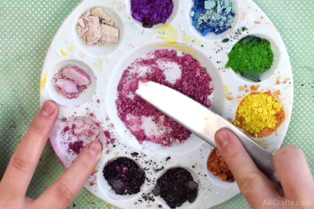 using a knife to smash pink eyeshadows in a mixing tray
