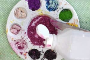 adding rubbing alcohol to pink eyeshadow in a mixing tray