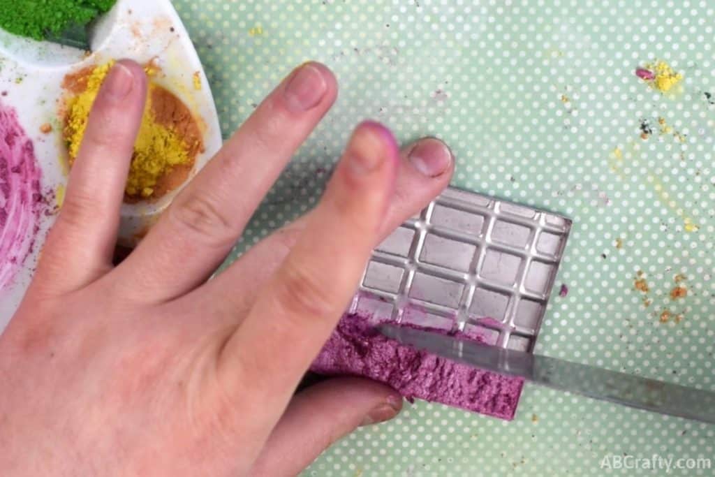 pushing pink eyeshadow paste with a knife to make it even in an eyeshadow pot