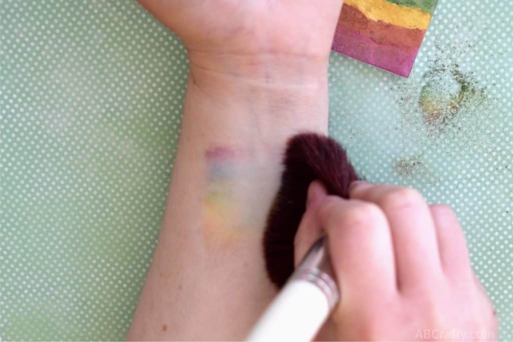 wiping rainbow makeup across the forearm with a makeup brush