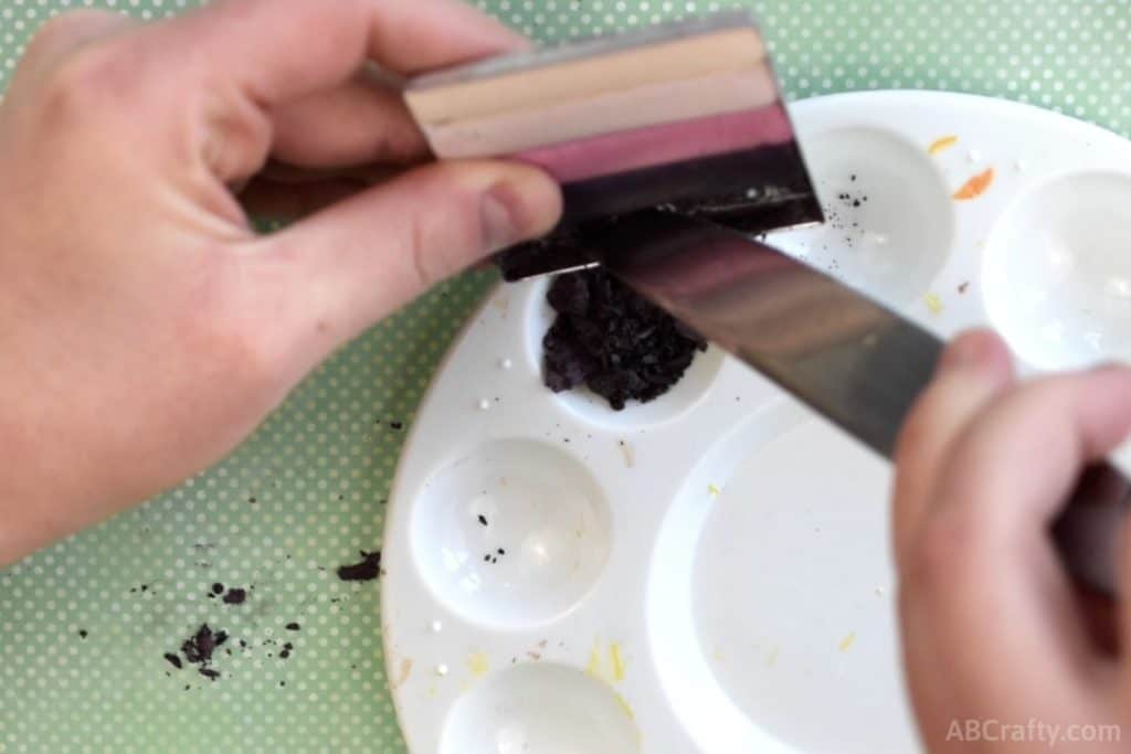 using a knife to scrape purple eyeshadow out of an eyeshadow palette